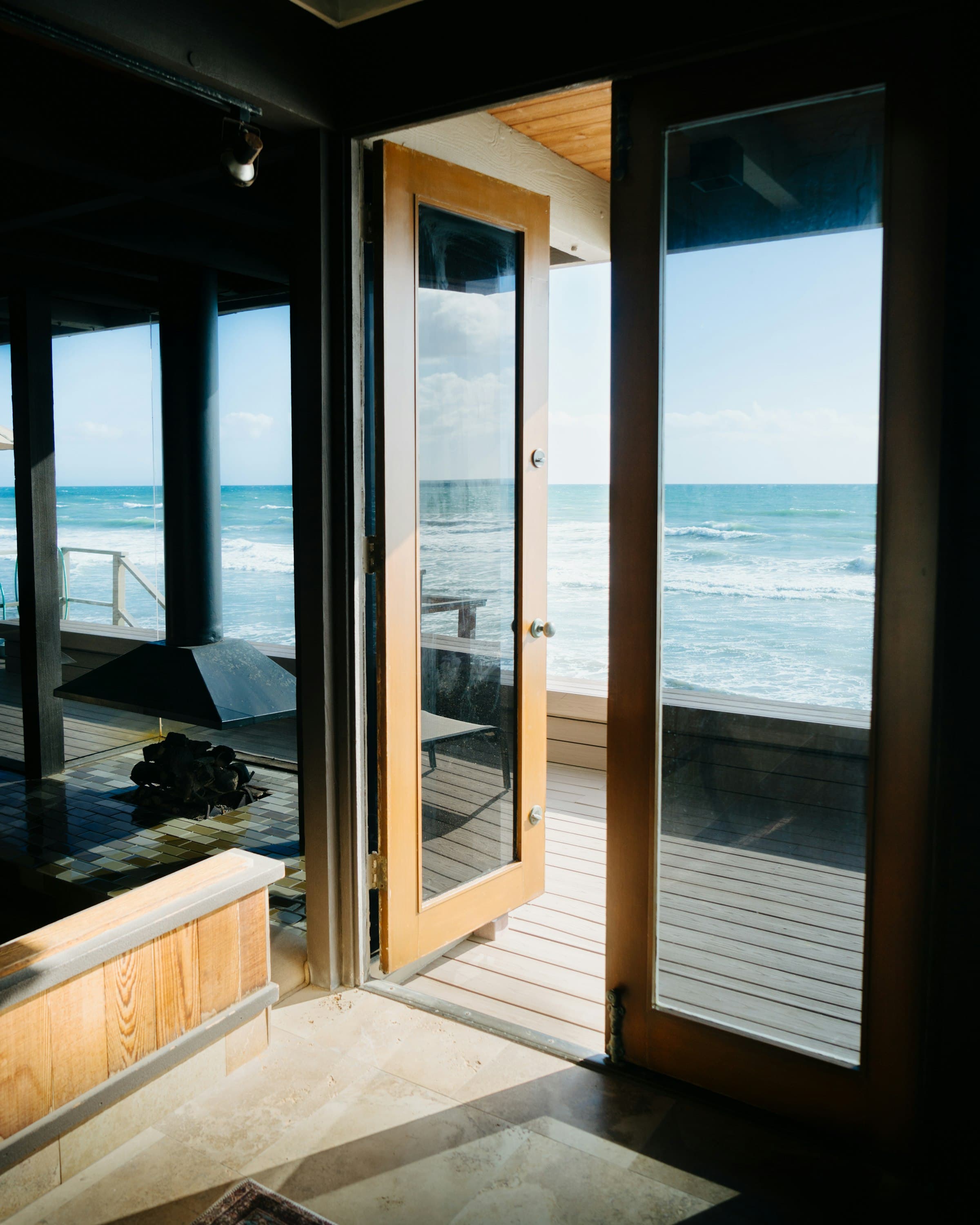Open wood-framed doors looking from a house onto a deck and the Pacific Ocean.